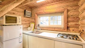 A log cabin kitchen with a refrigerator, microwave, sink, and gas stove.