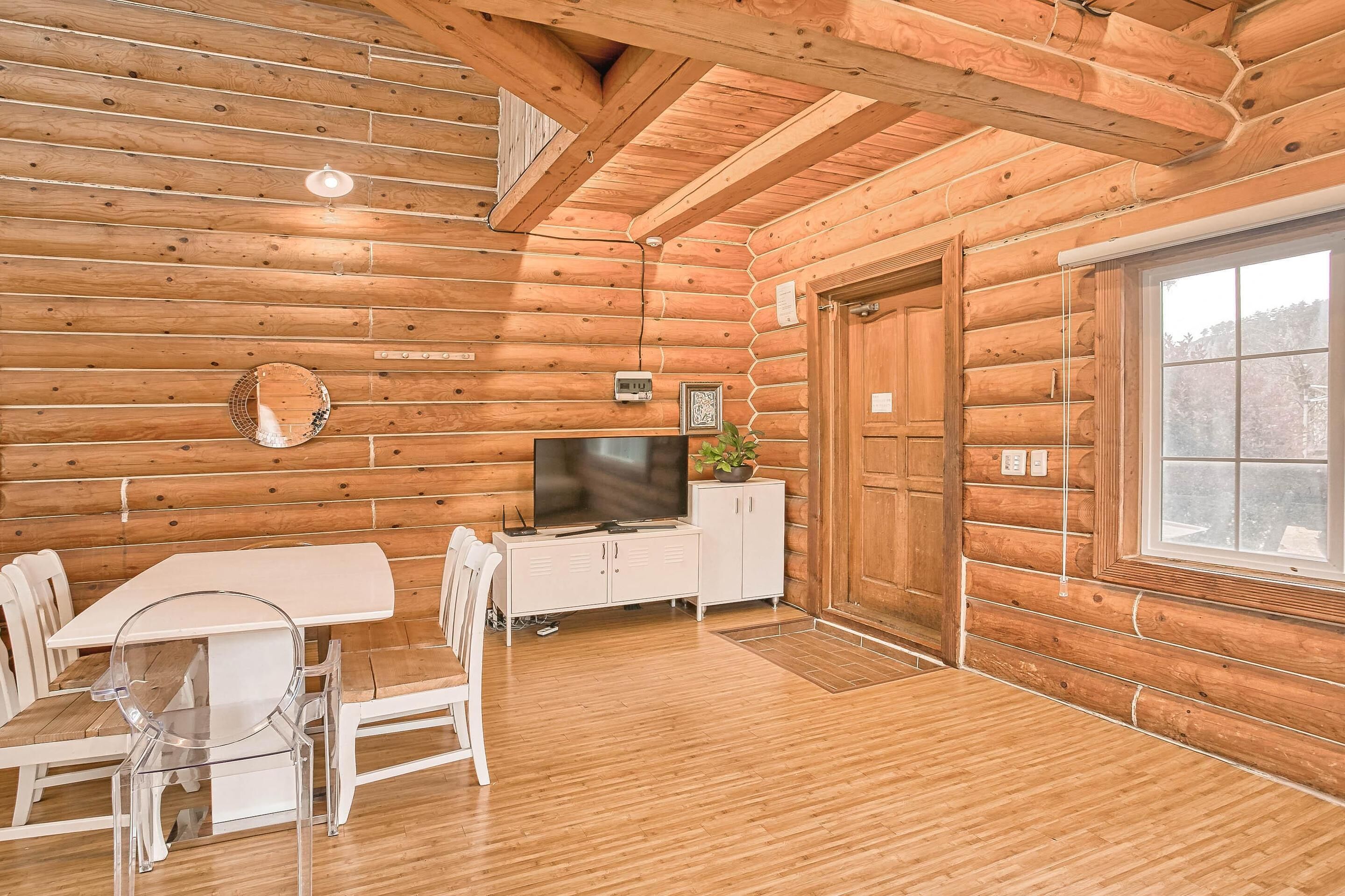 Interior de una cabaña de madera con una mesa de comedor, sillas, un televisor y un armario.