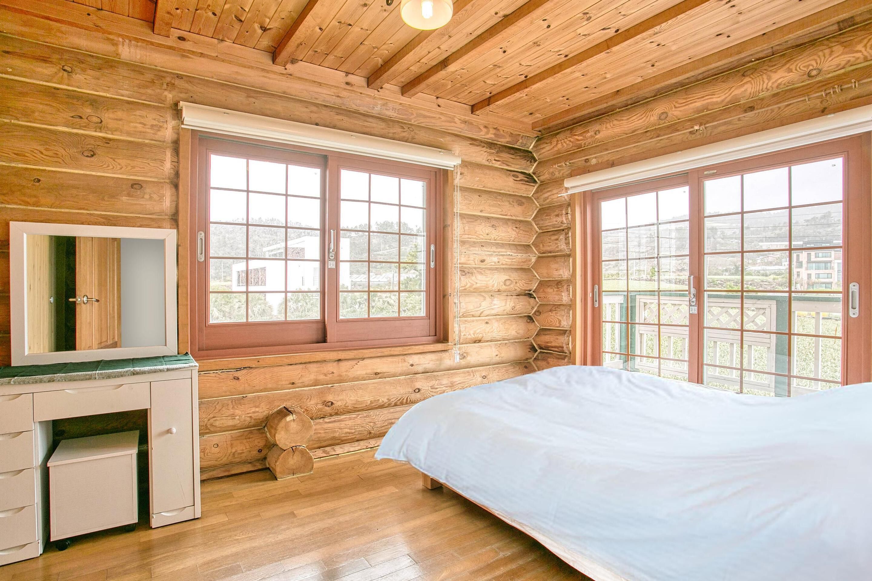 A log cabin bedroom with a bed, a dresser, and two windows with wooden frames.