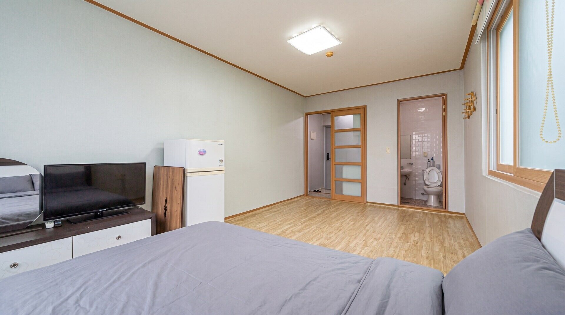 Een slaapkamer met een bed, een televisie, een kleine koelkast en een houten garderobe.