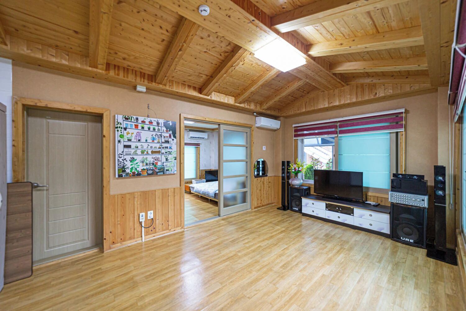 Una habitación con piso de madera, televisor, parlantes y una puerta corredera que conduce a otra habitación.