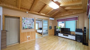 Una habitación con piso de madera, televisor, parlantes y una puerta corredera que conduce a otra habitación.
