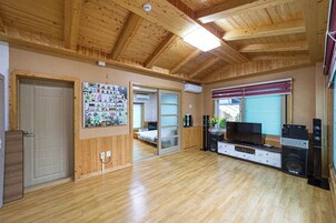 A room with wooden flooring, a television, speakers, and a sliding door leading to another room.