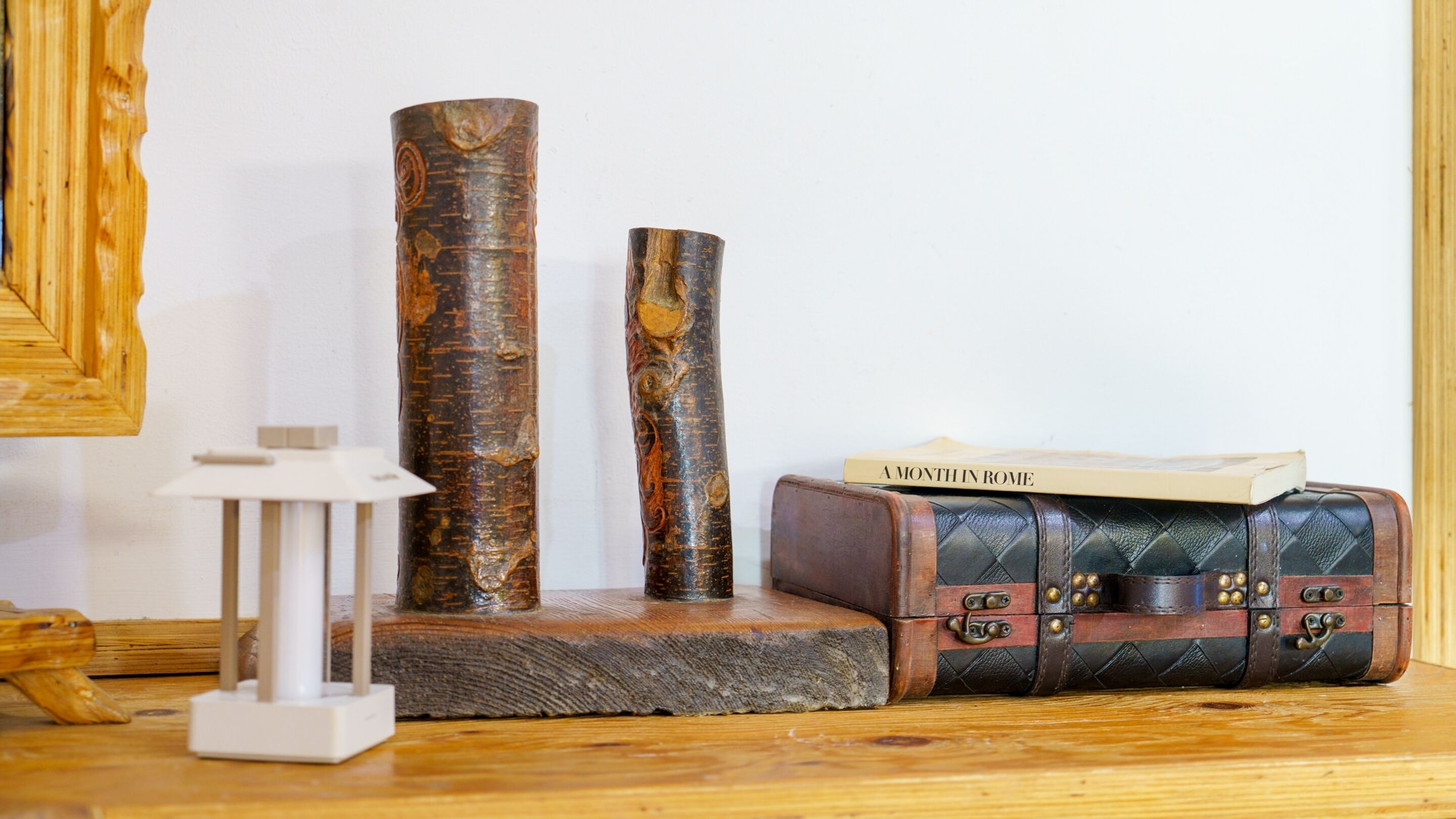 A wooden table with a white lamp, two cylindrical objects, and a vintage suitcase with a book on top.