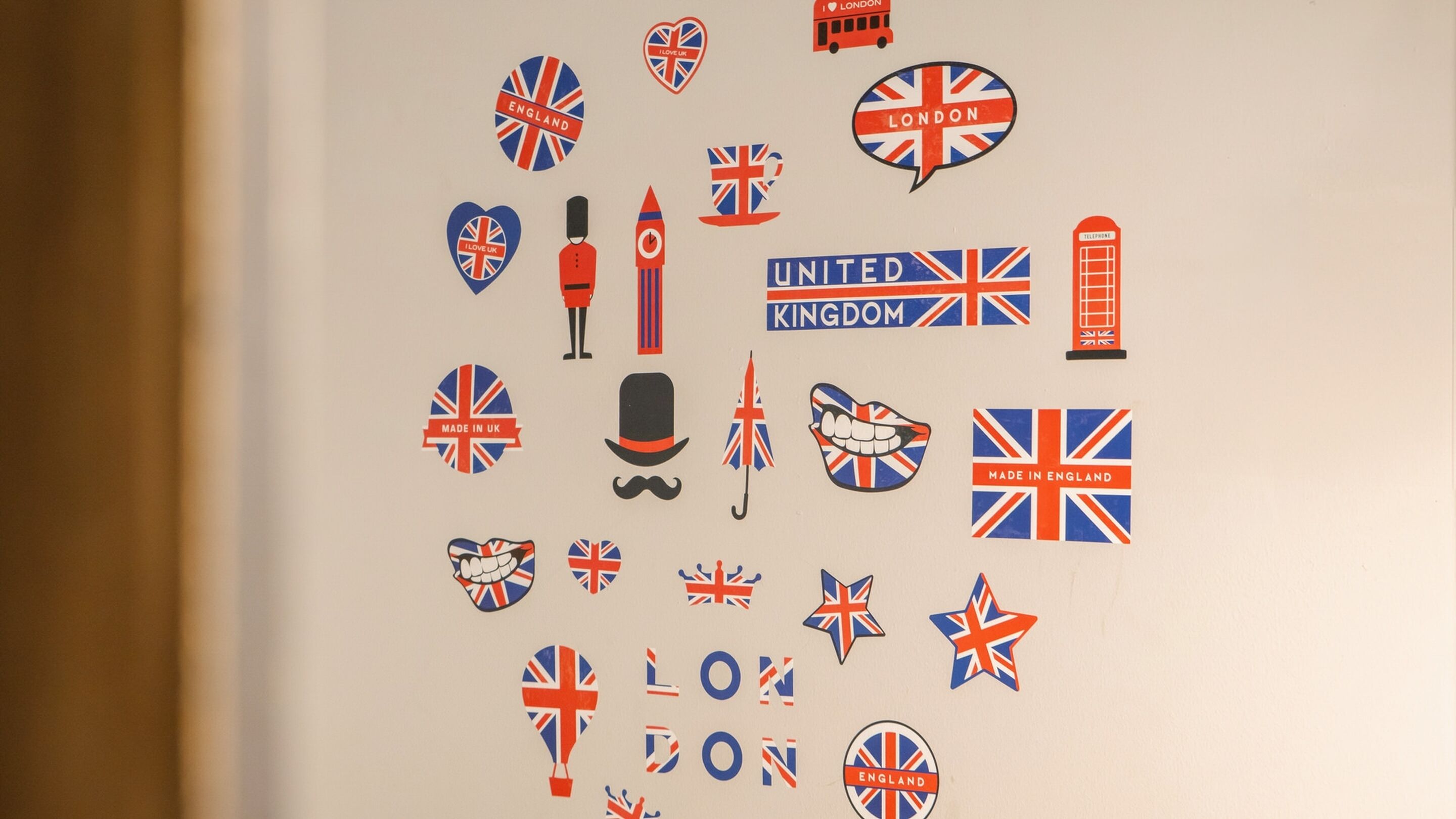 Een muur versierd met verschillende stickers en iconen uit het Verenigd Koninkrijk, waaronder de Union Jack, een rode telefooncel en een zwarte hoed.