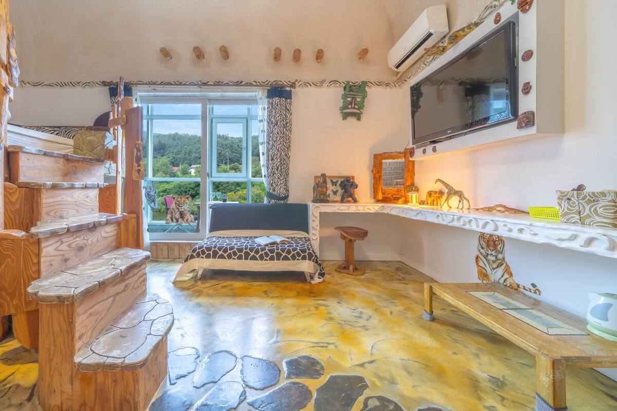 Una habitación con piso de diseño de piedra, una cama con colcha estampada, una escalera de madera y una ventana con vistas a zonas verdes.