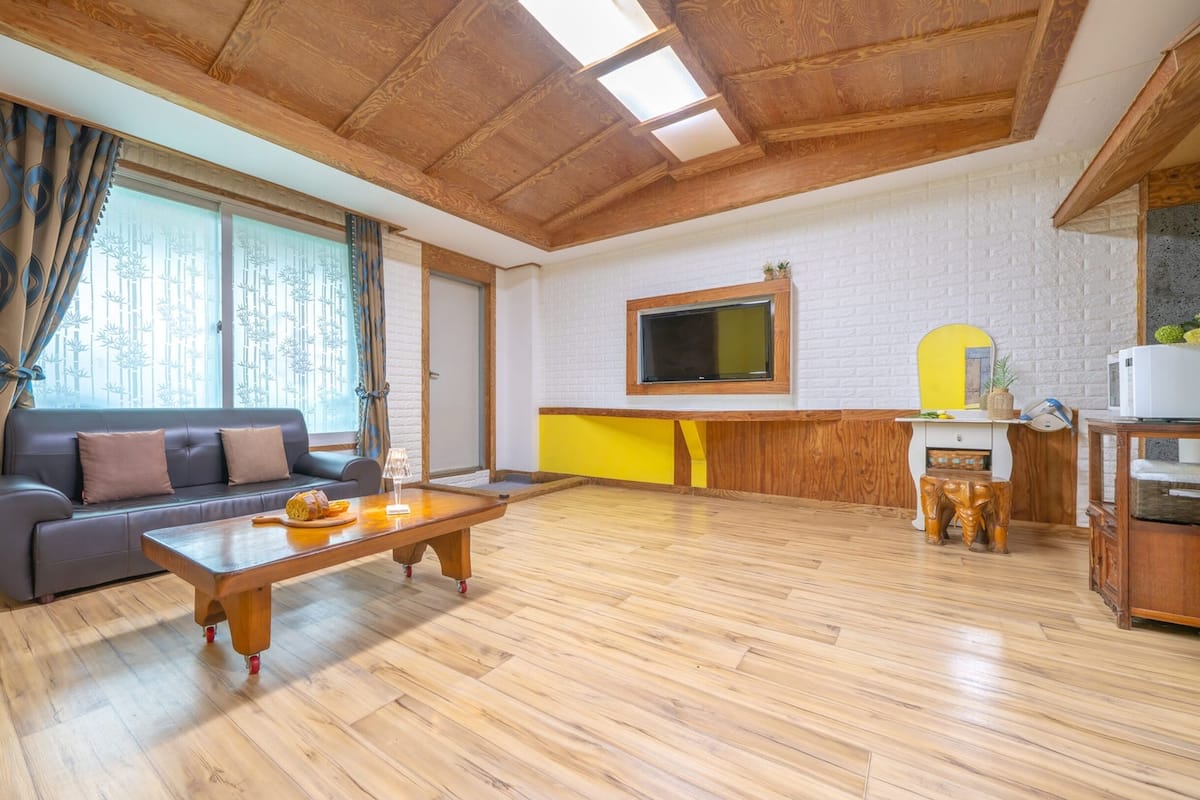Una sala de estar con un sofá, una mesa de centro de madera y una zona de cocina con microondas y un mueble amarillo.