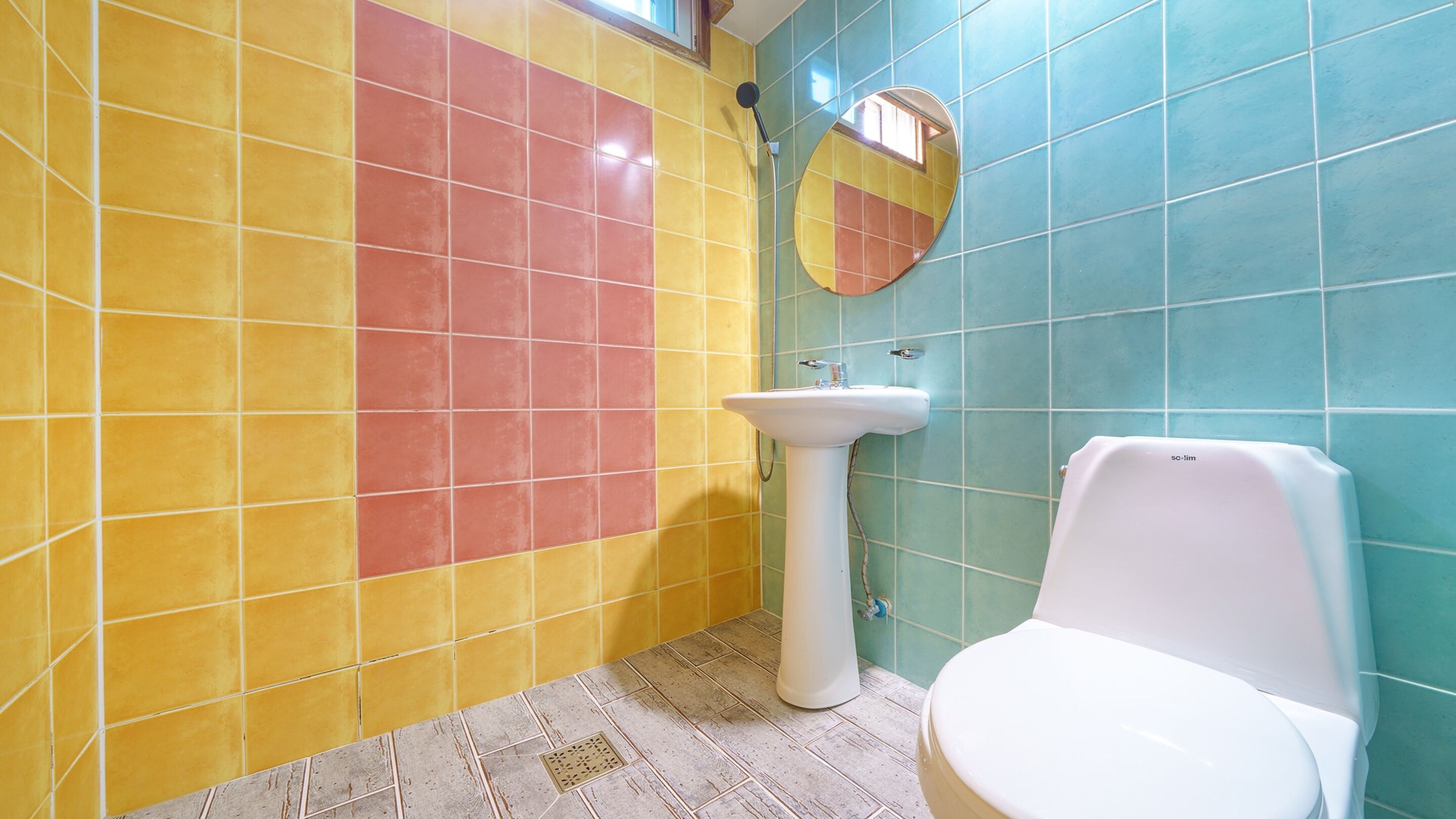 A bathroom with a white sink, a toilet, and a mirror on the wall. The walls are tiled in yellow, red, and blue.