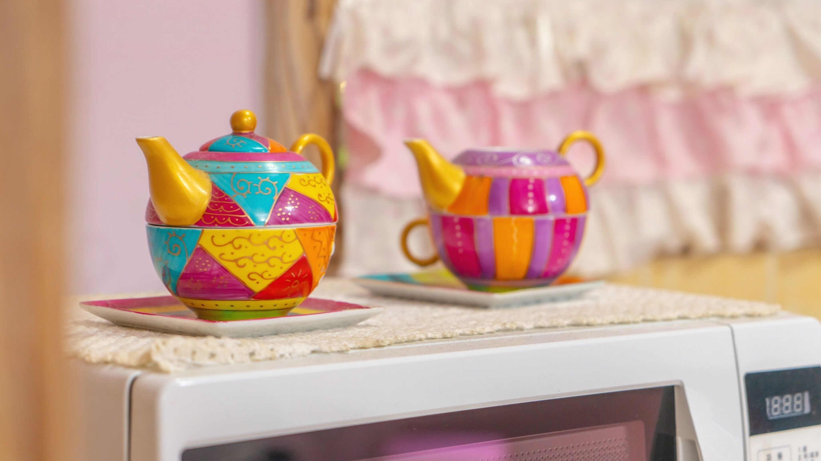 Two colorful teapots on a microwave.