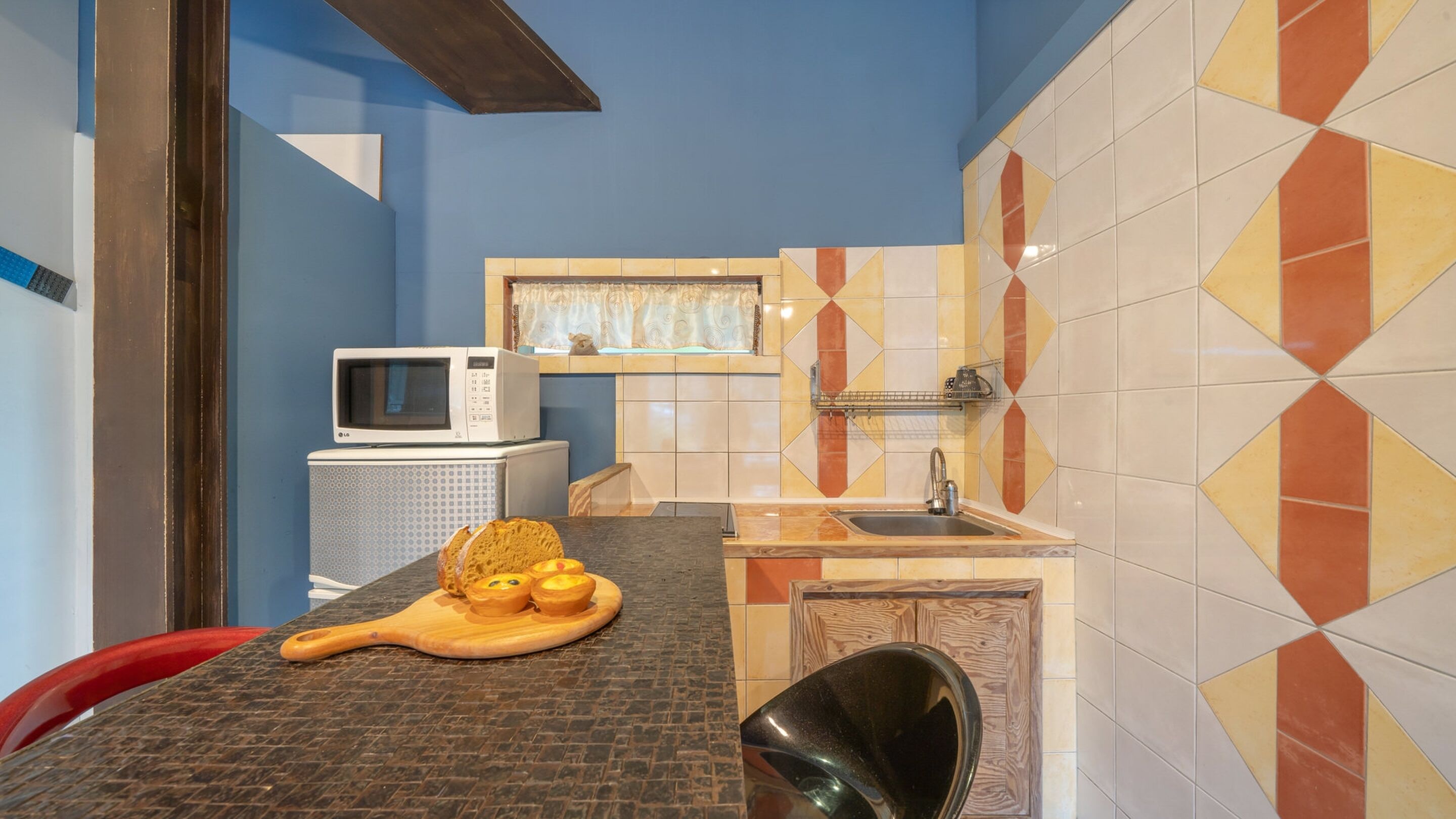 A compact kitchen with a microwave, a sink, and a wooden cutting board with bread.