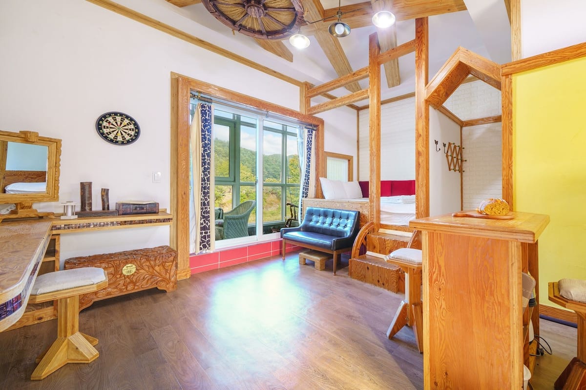 Una habitación rústica con techo de madera, un ventanal con vistas, un dardo y una cama con cabecera roja.