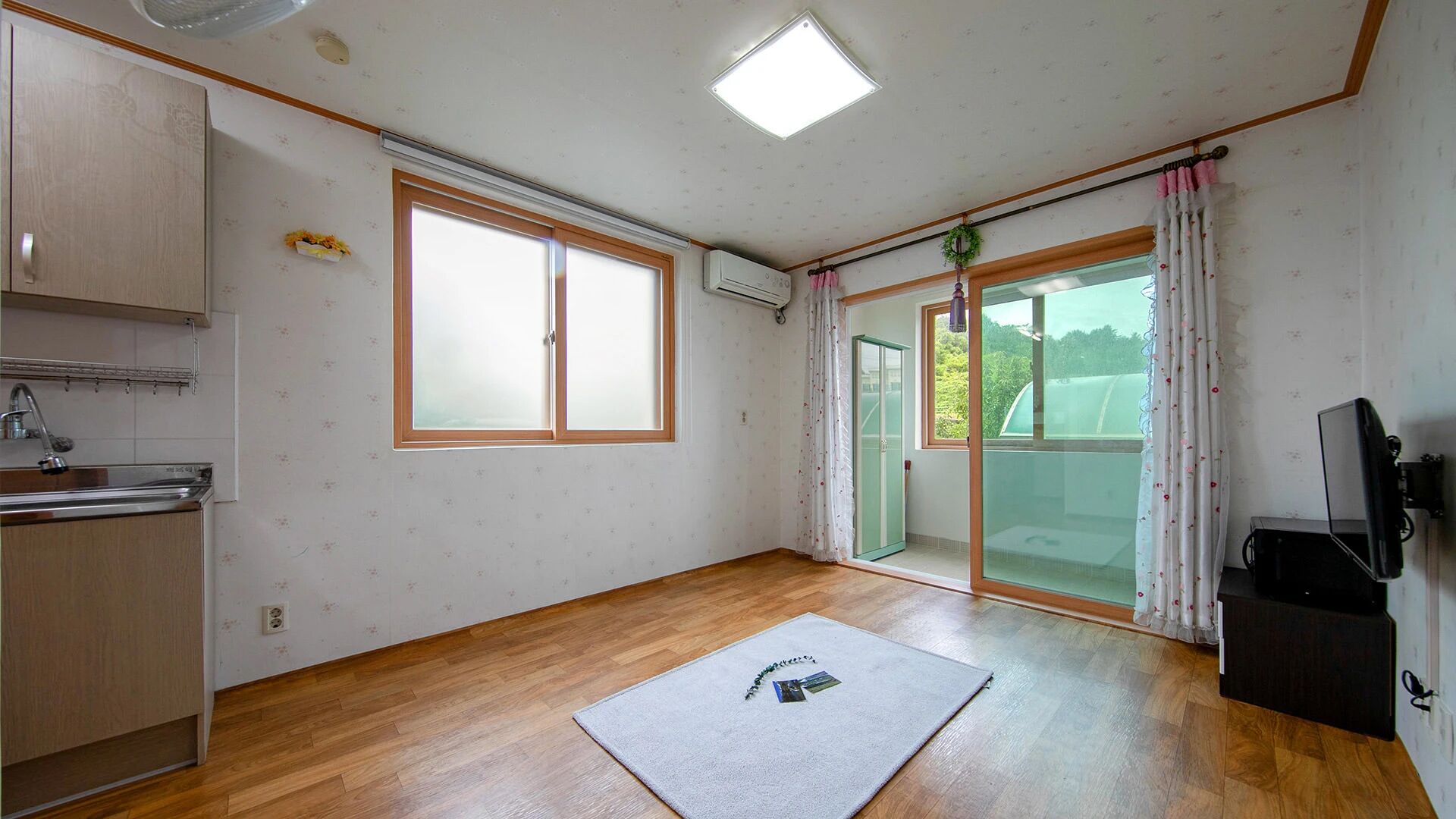 A room with a kitchenette, a large sliding glass door to a balcony, and a flat-screen TV.