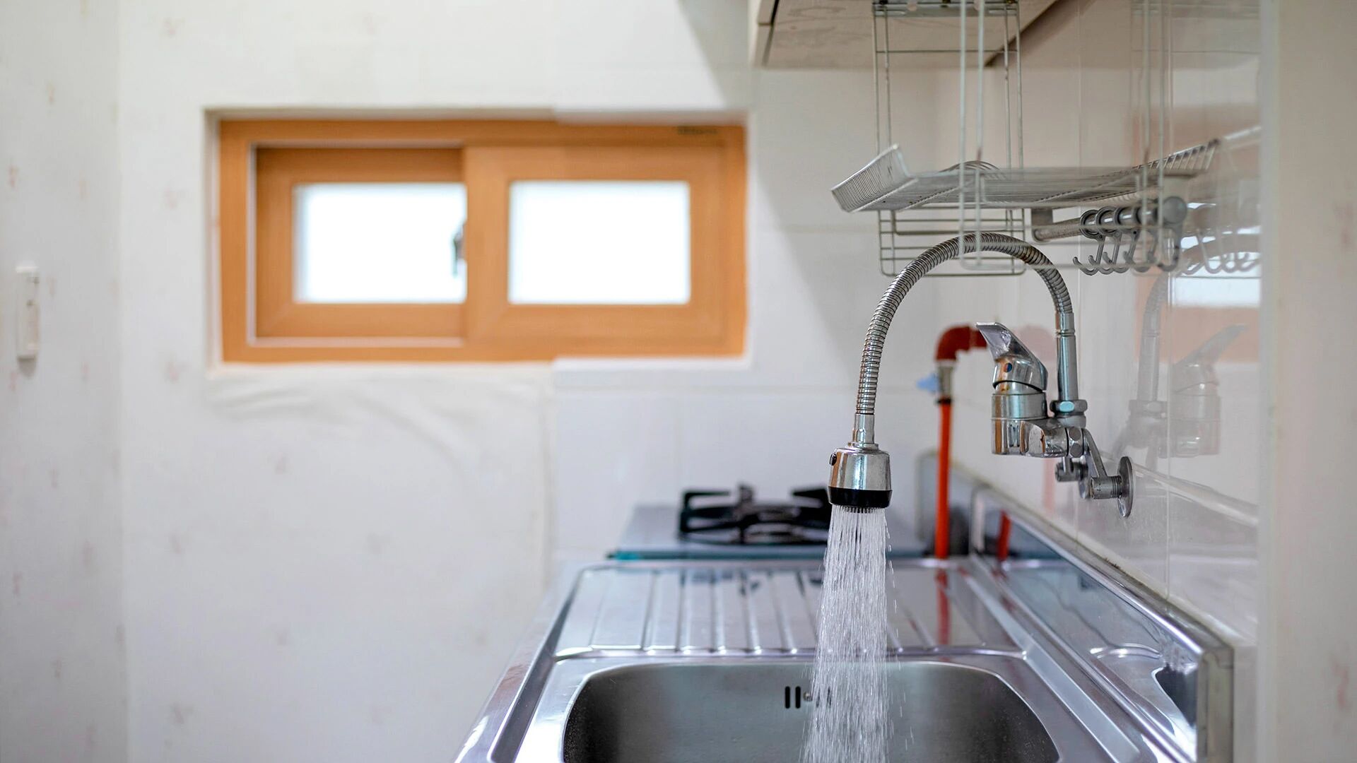 Un lavamanos de cocina con grifo, una ventana encima y una repisa metálica en la pared.