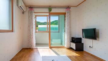 A room with a wooden floor, a sliding glass door leading to a balcony, a flat-screen TV, and a small black cabinet.