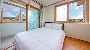 Un dormitorio con una cama, dos ventanas y vistas a edificios.