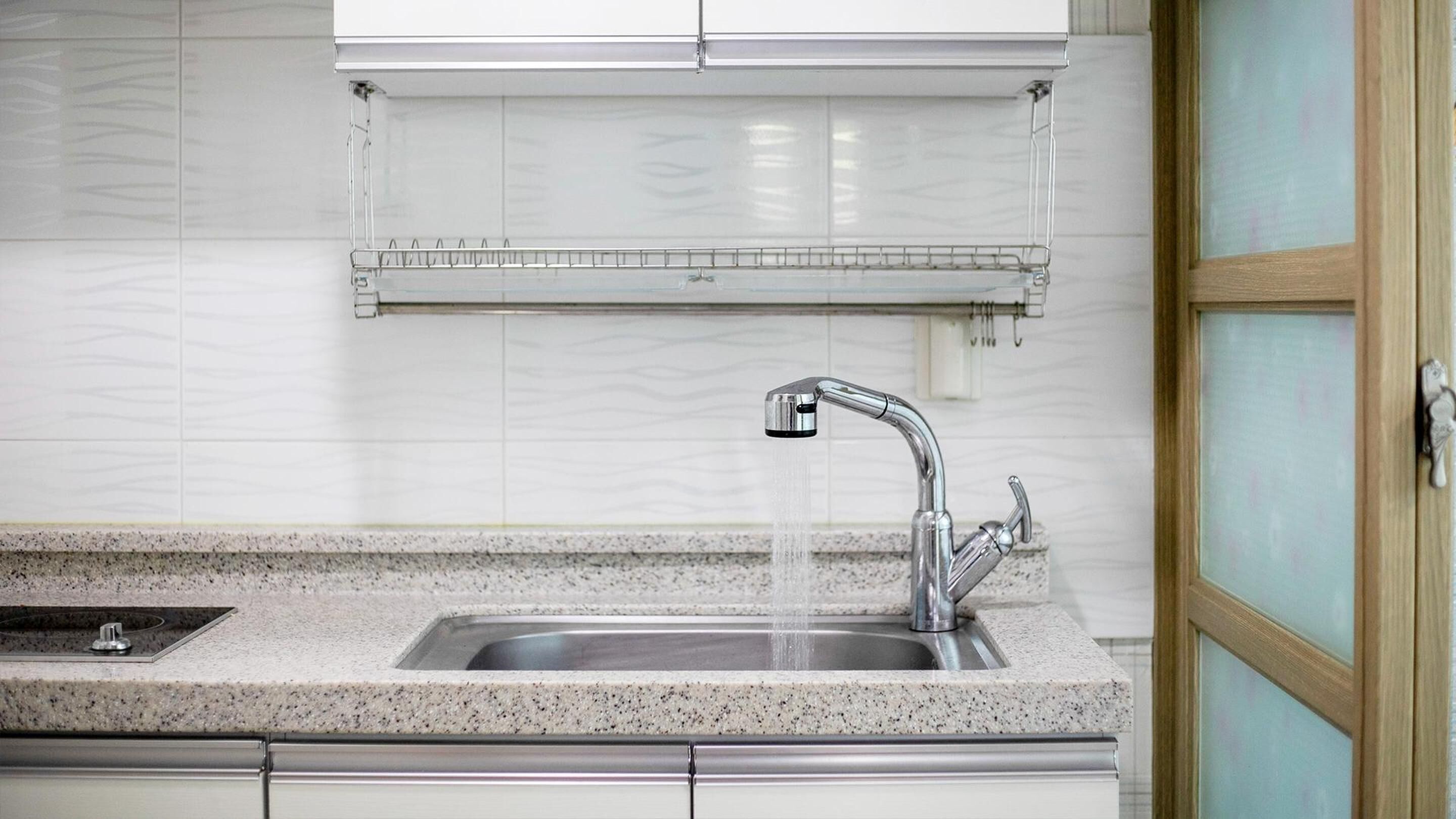 Una cocina con encimera de granito, pileta de acero inoxidable y salpicadero de azulejos blancos.