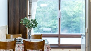 Un comedor con una mesa dispuesta para cuatro personas, un florero con follaje verde y una ventana con vistas a árboles.