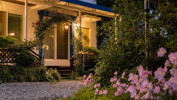 A house with a covered porch, a well-maintained garden, and a gravel pathway.