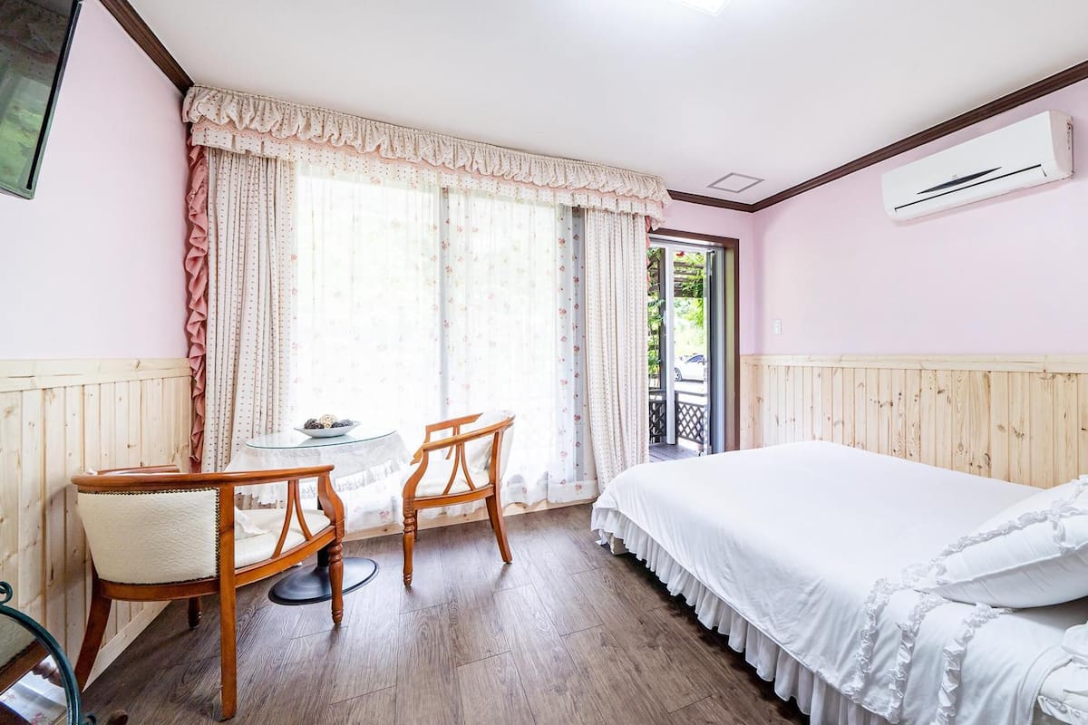 A bedroom with a bed, a small table, two chairs, and a window with curtains.