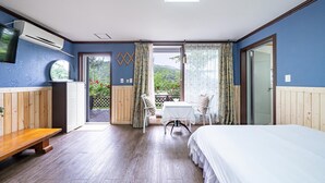 Un dormitorio con cama, una pequeña mesa con sillas, televisor y balcón con vistas a zonas verdes.