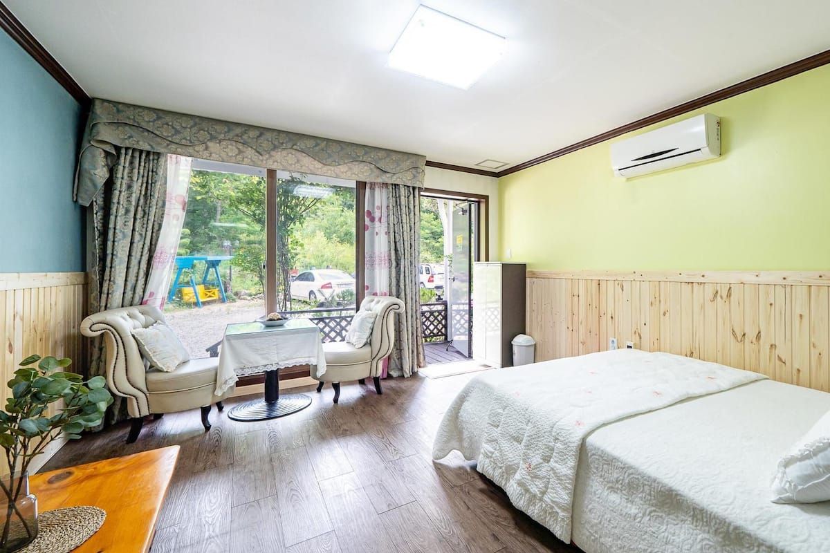 A hotel room with a bed, a sofa, a small table, and a window with a view of the outside.