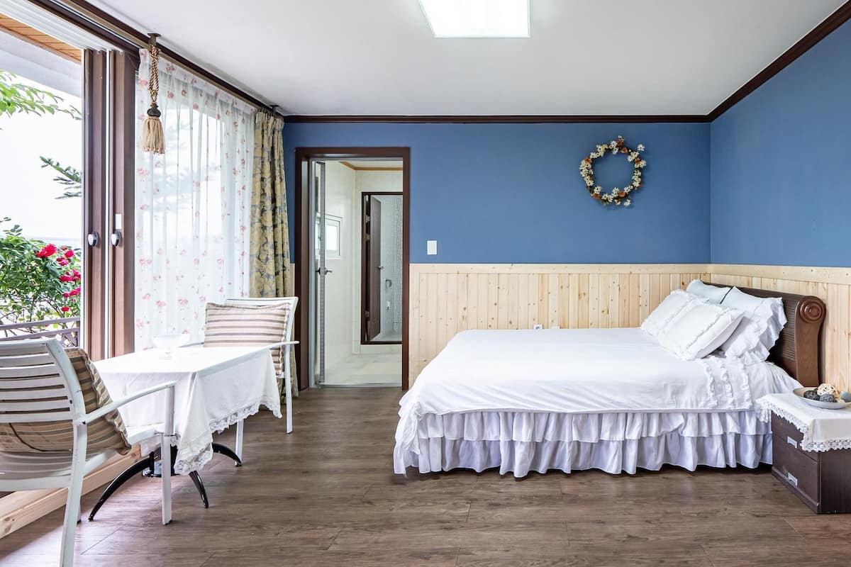 A bedroom with a bed, a table, and a chair. There is a door leading to another room.