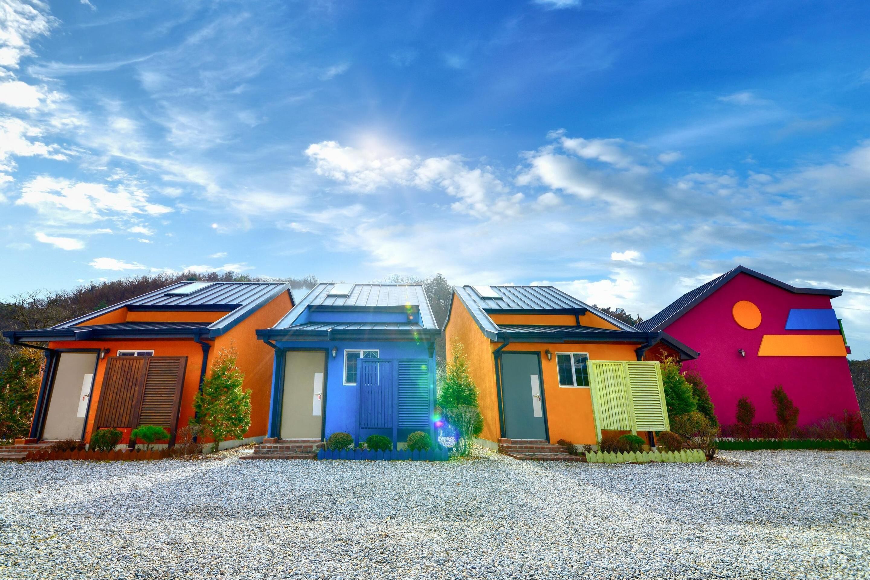 A modern house with a gravel driveway, a blue door, and a colorful exterior.