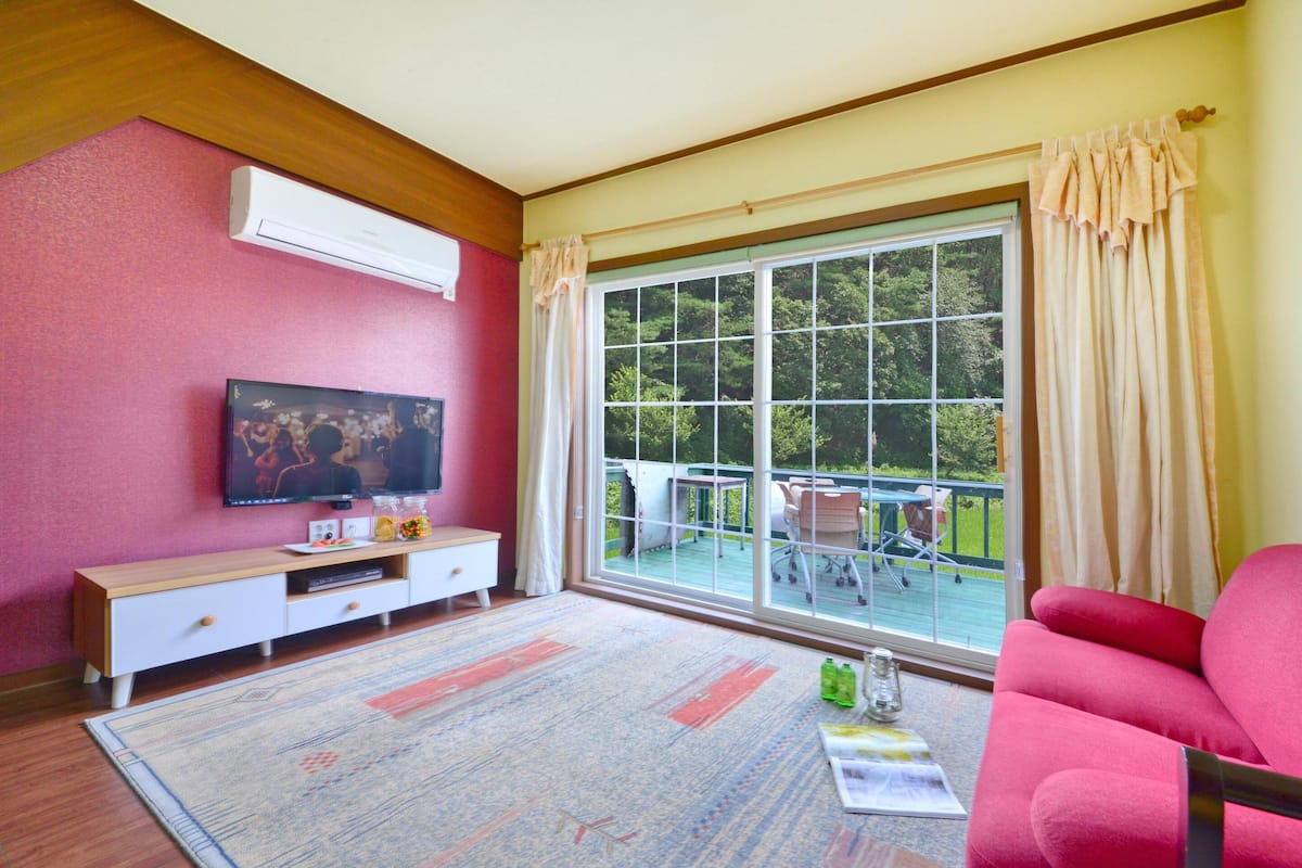 A living room with a large window, a flat-screen TV, a wooden entertainment unit, and a pink sofa.
