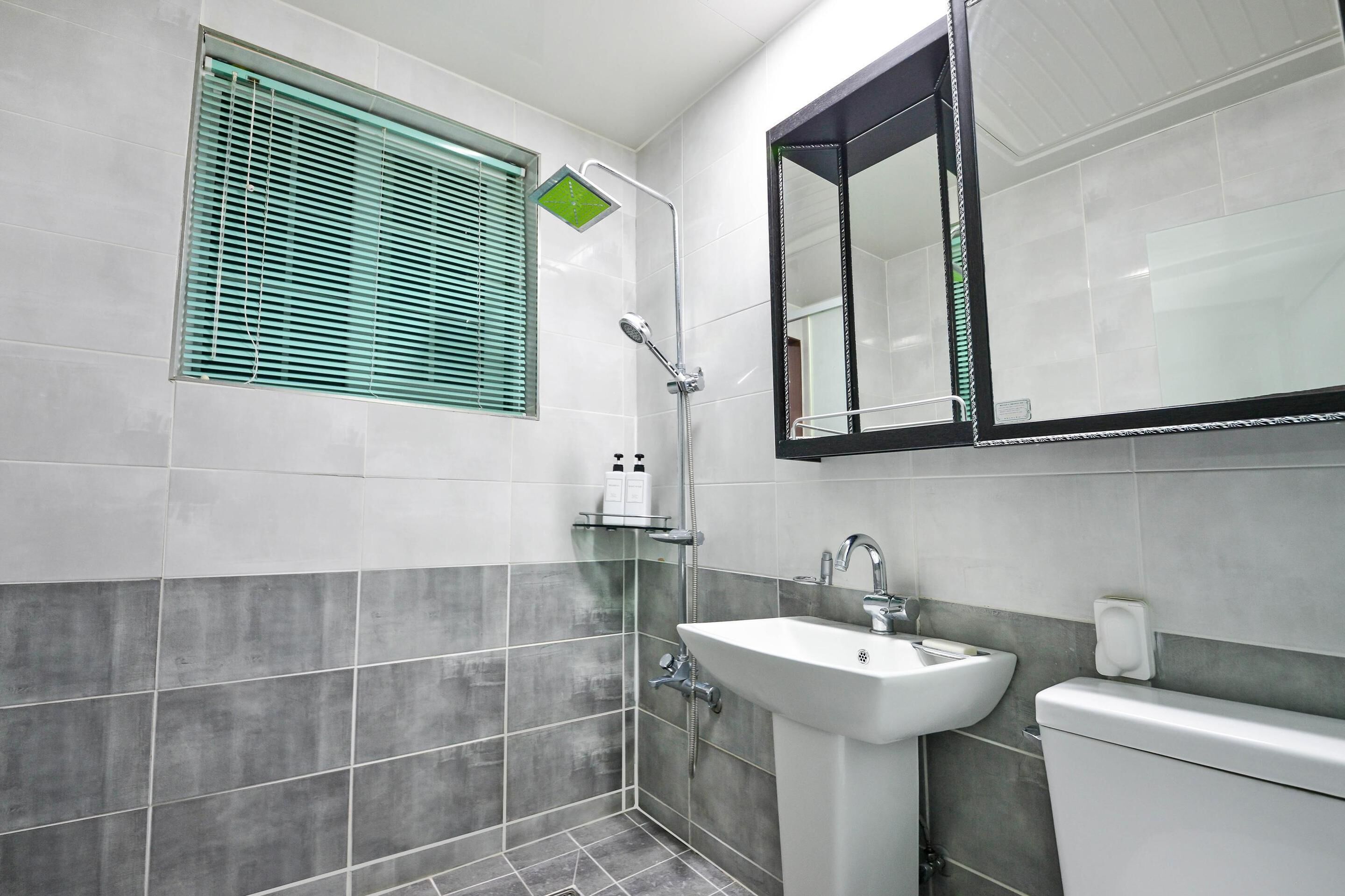 A bathroom with a shower, sink, toilet, and a window with blinds.