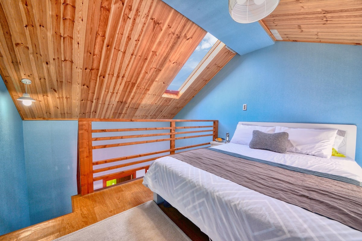 A bedroom with a sloped ceiling, a skylight, a bed with white bedding, and a wooden headboard.