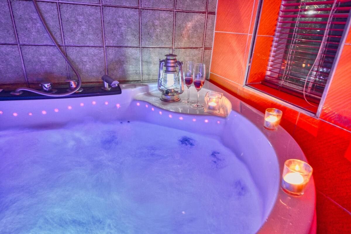 A hot tub with a lantern, candles, and glasses of red wine.