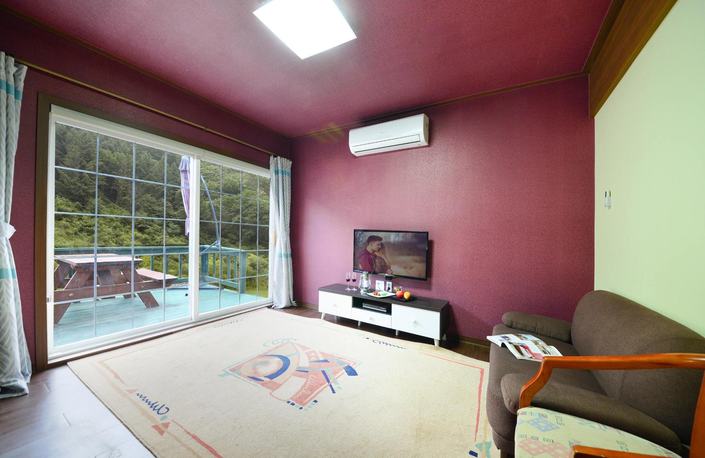 Ein Wohnzimmer mit großem Fenster, einer Couch, einem Fernseher und einem kleinen Tisch.