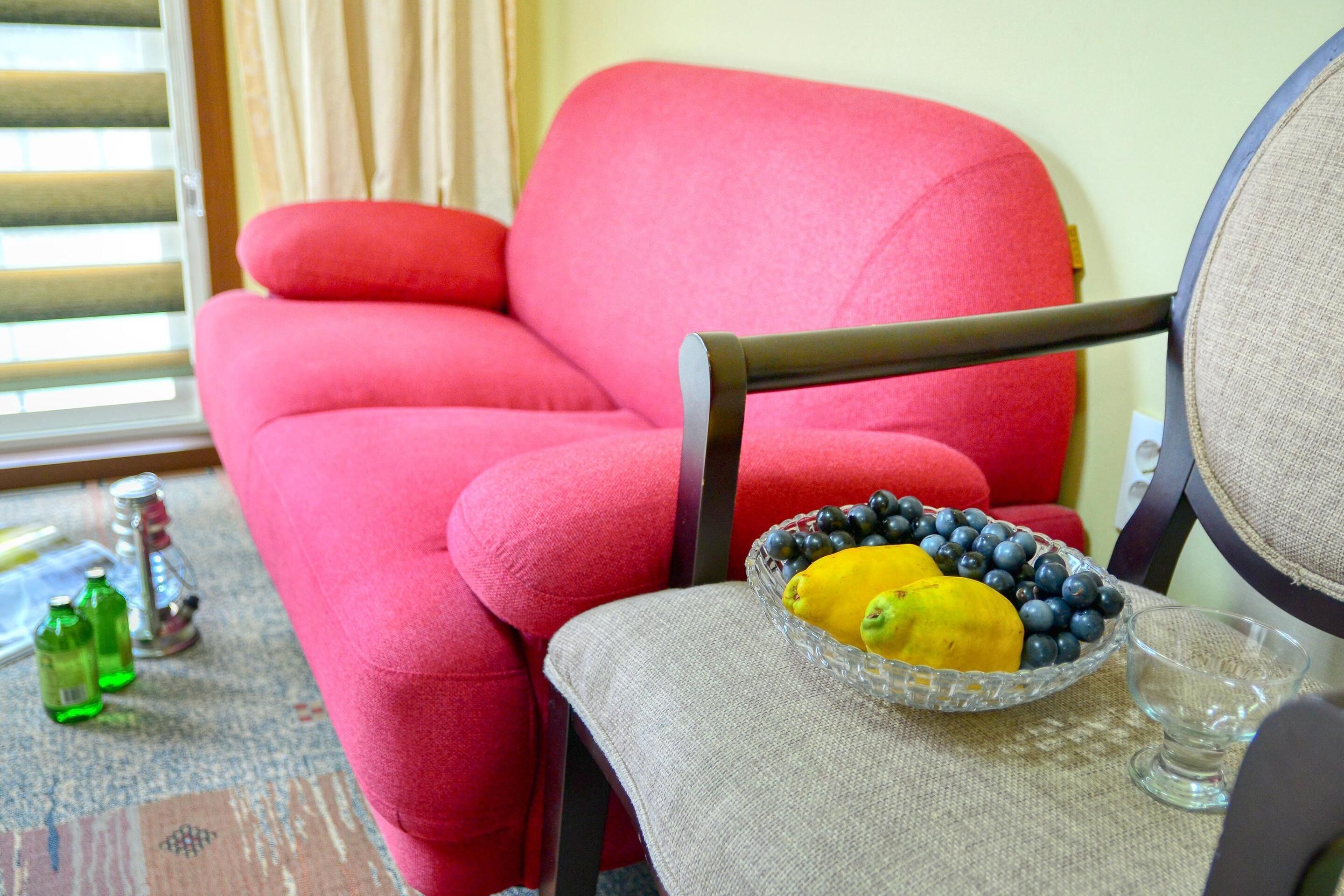 A red armchair with a glass bowl of fruit on a table.