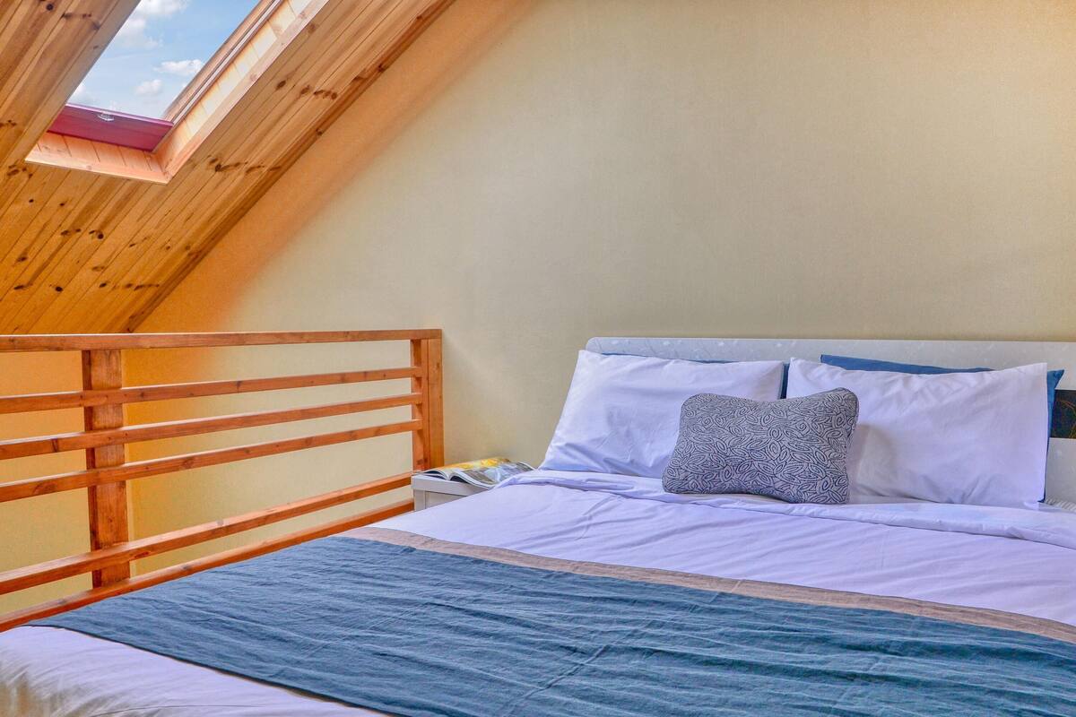 A bedroom with a sloped ceiling, a wooden headboard, a bed with white bedding, and a skylight.