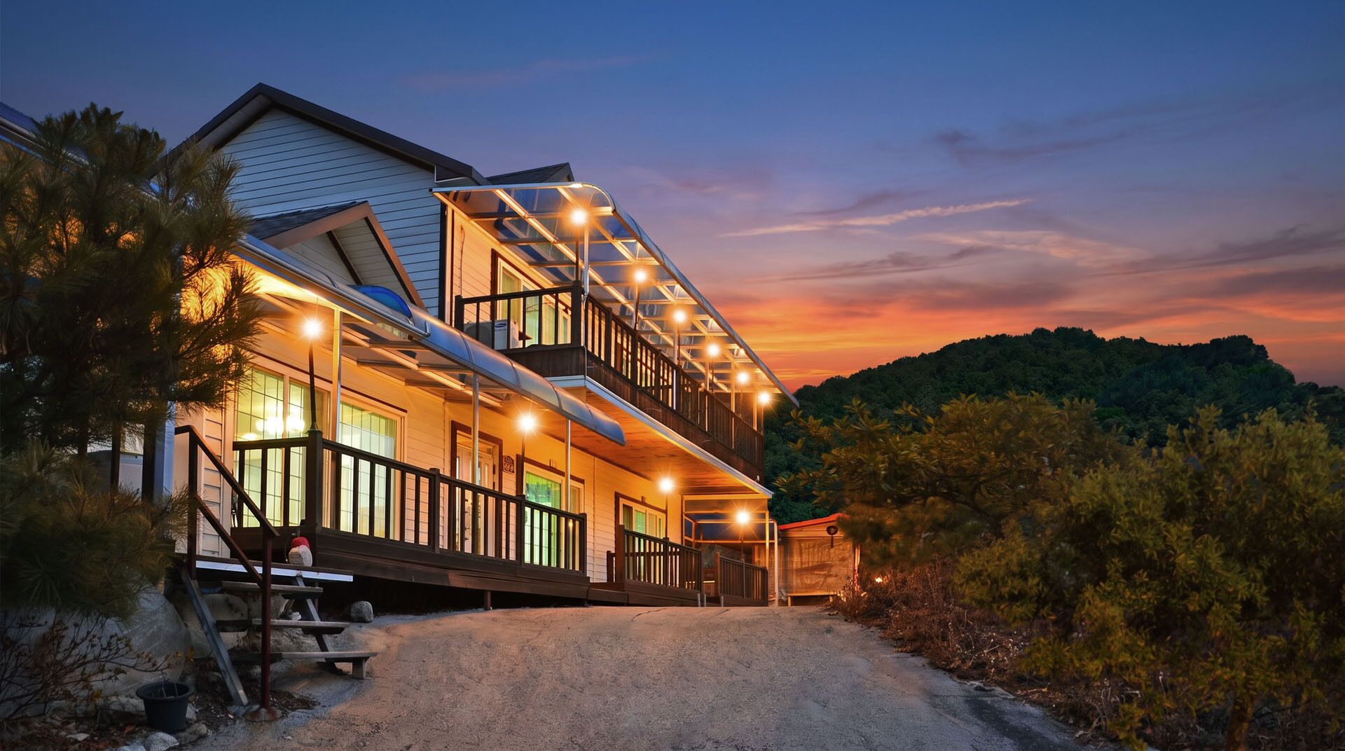A two-story house with a balcony, a covered porch, and a view of a forested hill.