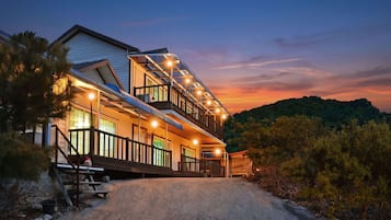 A two-story house with a balcony, a covered porch, and a view of a forested hill.