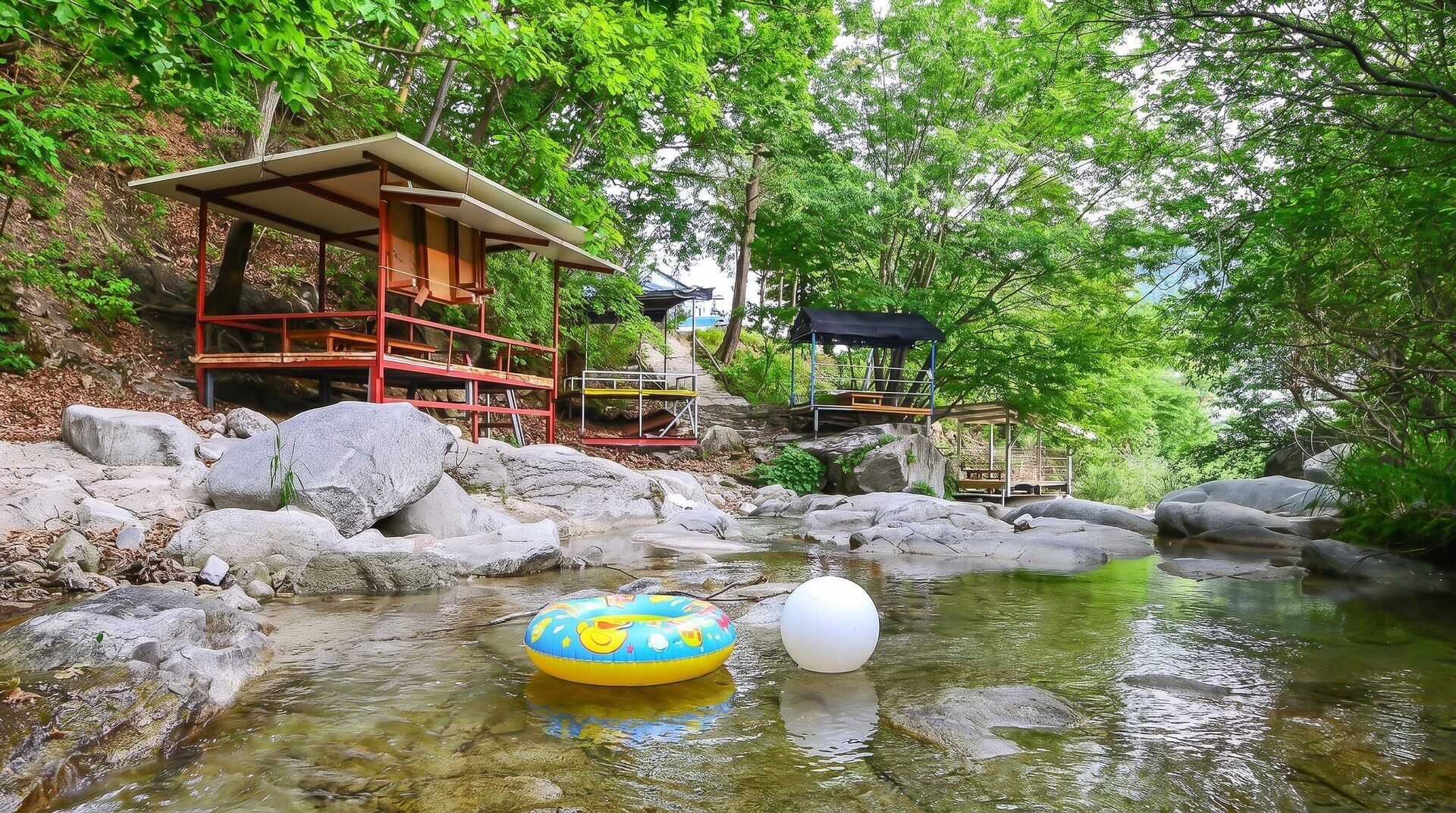 Un cadre naturel avec un ruisseau aux eaux claires, des rochers et des structures en bois.