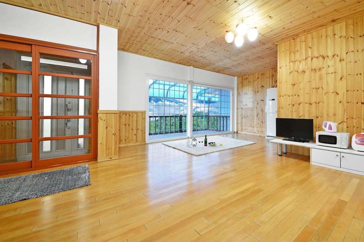 A spacious room with wooden flooring, a large sliding glass door, a flat-screen TV, a microwave, and a small refrigerator.