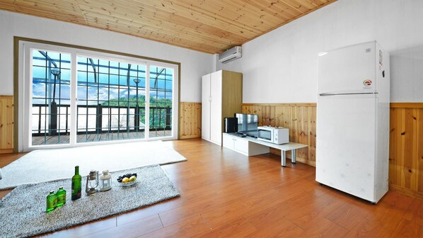 Ein geräumiger Raum mit einem großen Schiebeglastür, die auf einen Balkon führt, sowie einem weißen Kühlschrank, einer Mikrowelle, einem Fernseher und einem Holzboden.