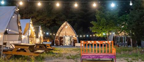 A campsite with tents, a wooden bench, and string lights.