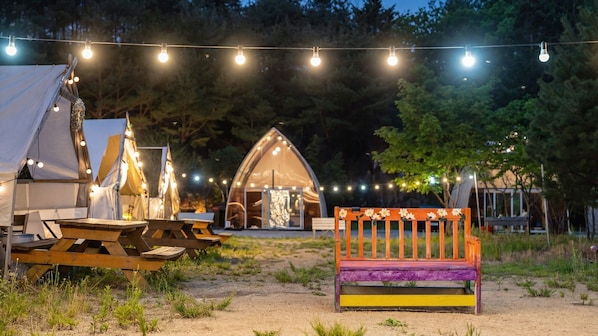 Ein Campingplatz mit Zelten, einer Holzbank und Lichterketten.
