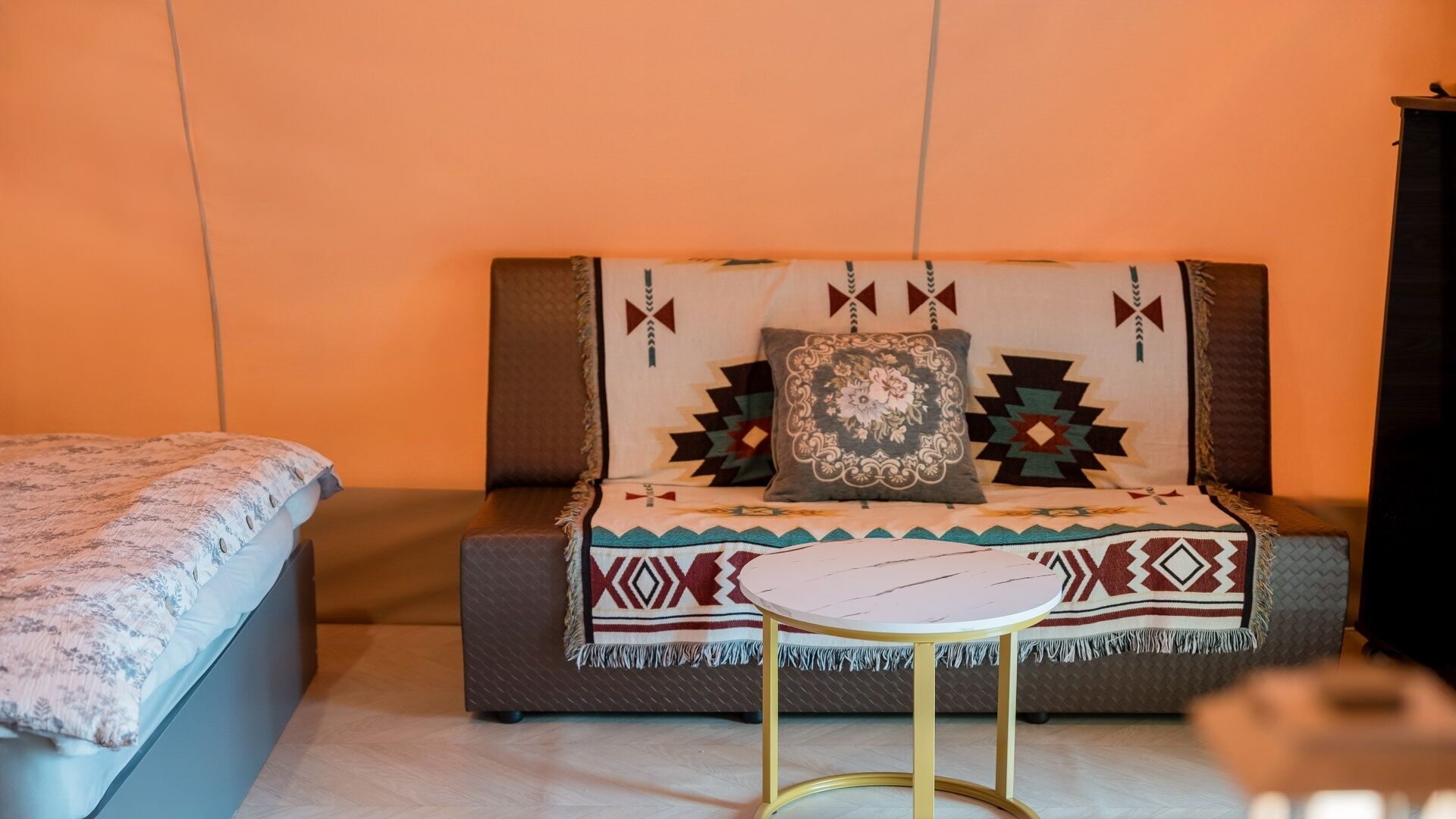 Quarto com cama, sofá, mesa redonda pequena e manta estampada.