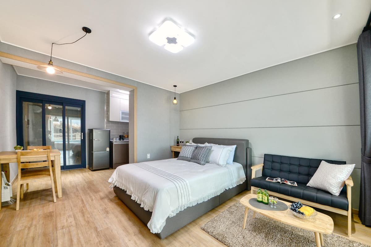 A modern bedroom with a bed, a sofa, a dining table, and a kitchen area.