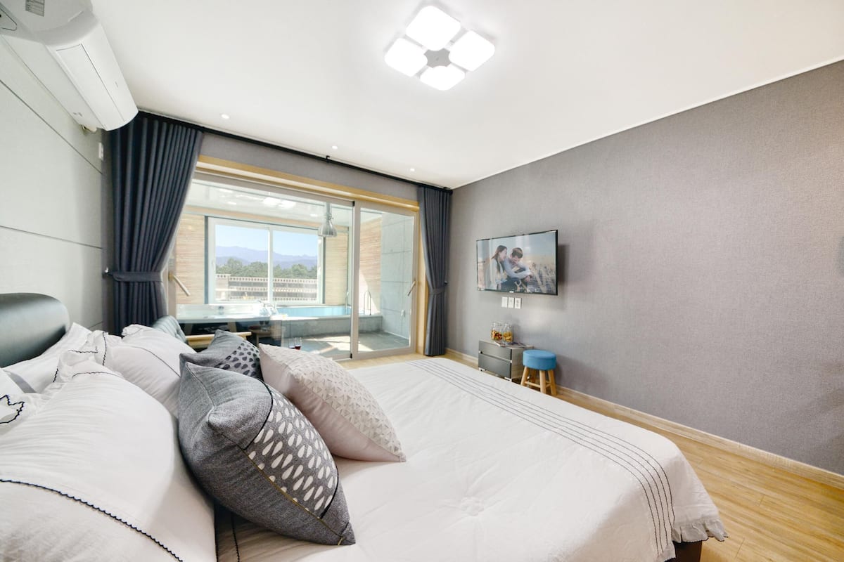 A modern hotel room with a large bed, a TV, a balcony with a view, and a sliding glass door.