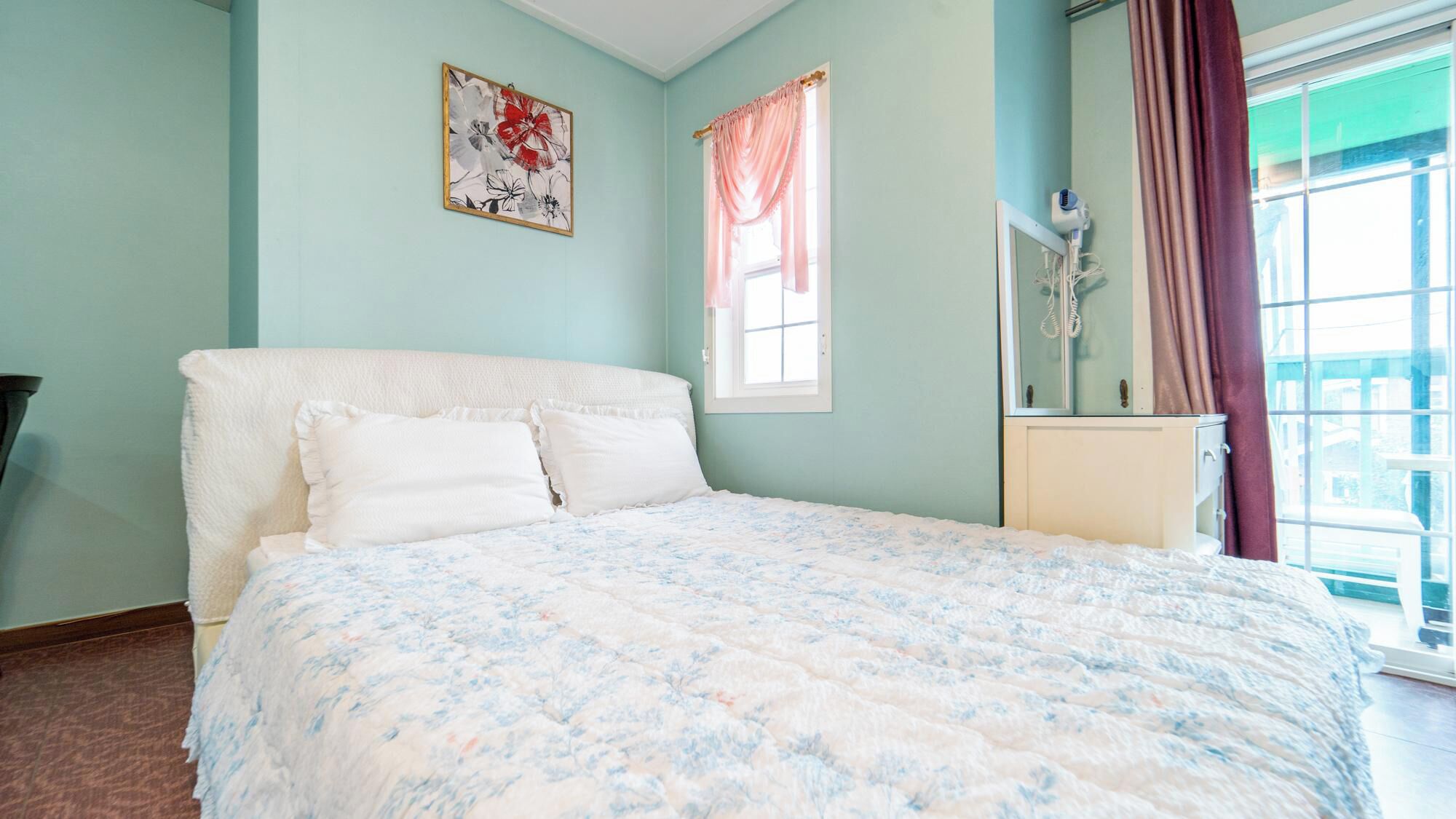 A bedroom with a bed, a window with curtains, a bedside table, and a wall-mounted air purifier.