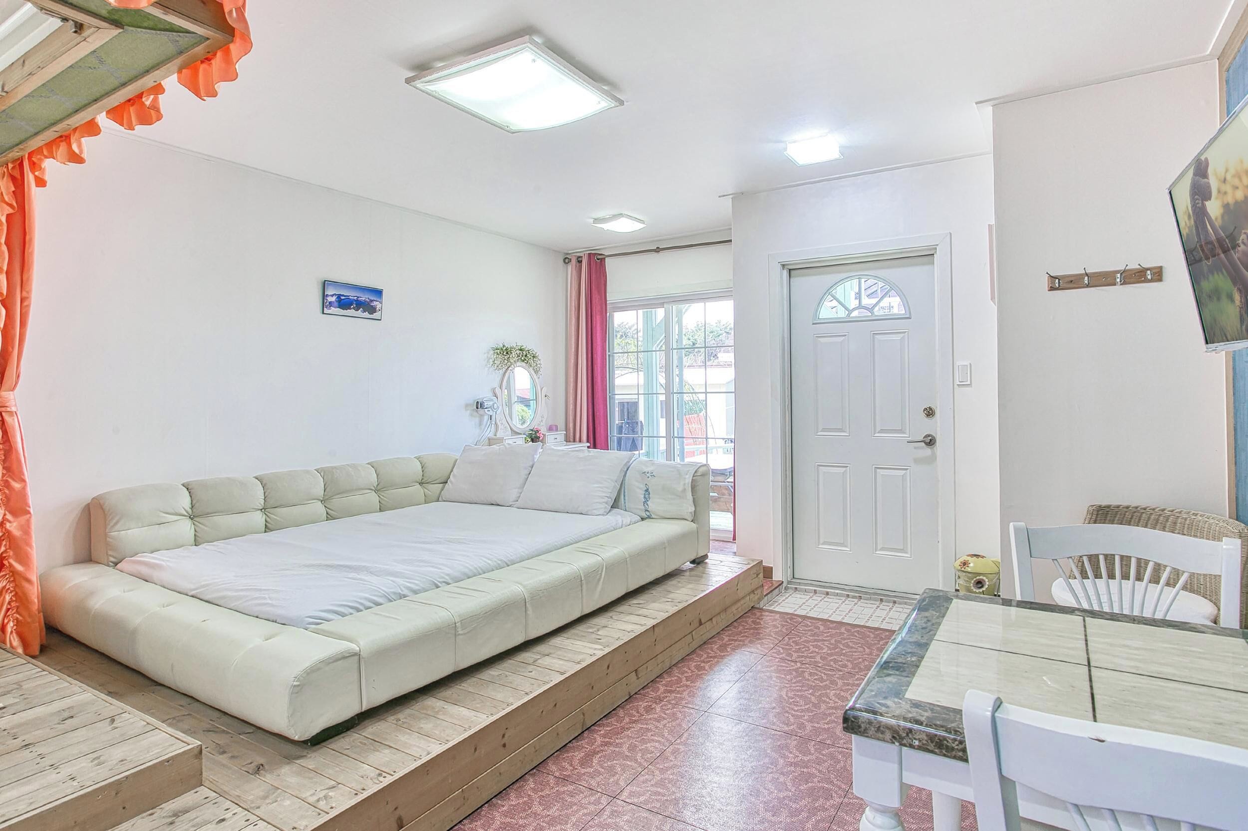 A bedroom with a large bed, a dining table, and a door.