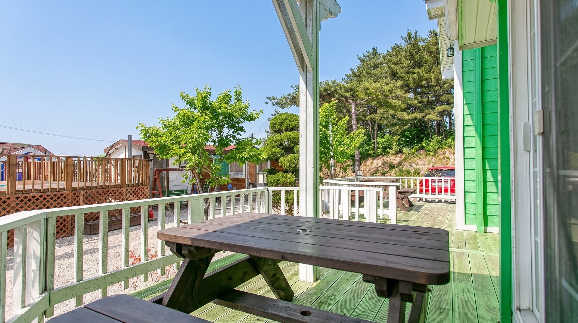 Eine Holzterrasse mit Picknicktisch, umgeben von einem weißen Geländer und Blick auf eine Wohngegend mit Häusern und Bäumen.
