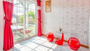 A room with a large glass door, red curtains, a glass table with two red stools, and a patterned wallpaper.