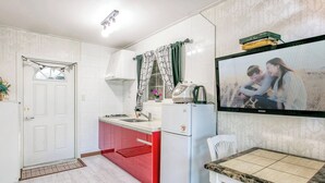 A kitchen with white cabinets, a red countertop, a white refrigerator, and a wall-mounted TV displaying a family photo. - Youngheungdo Roma Spa Pension (Incheon)