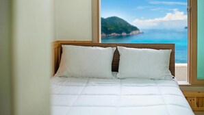 A bed with white bedding and a wooden headboard, positioned next to a window with a view of a coastal landscape. - Samcheok Haega Pension (Samcheok)